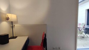 Une pièce avec un radiateur blanc, un bureau avec une lampe et une chaise rouge.