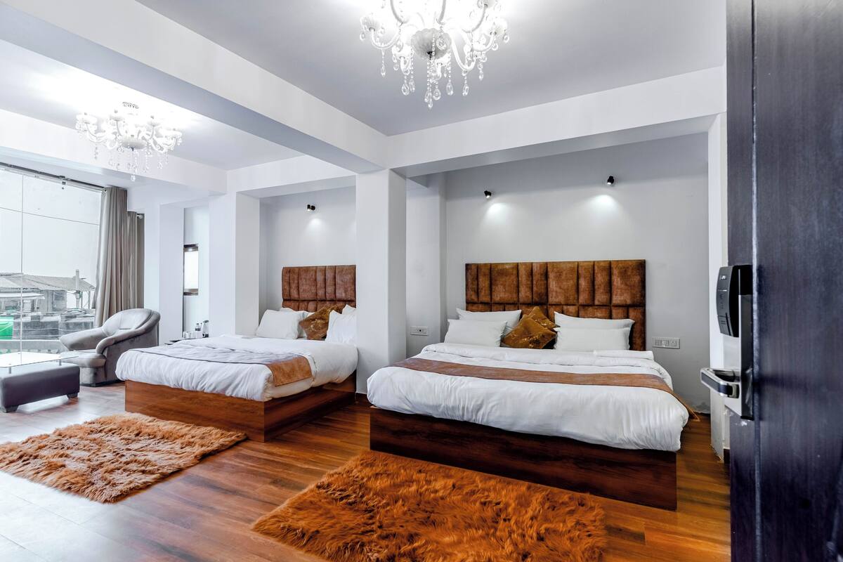 Moderni hotellihuone, jossa on kaksi sänkyä, suuri kattokruunu, iso ikkuna ja näkymä kaupunkiin.