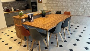 A modern kitchen with a wooden dining table, chairs, and a stone wall. - La Bergerie Maison Ancienne Rénovée (Villacerf)