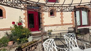 A covered patio with a red door, white chairs, and potted plants. - La Bergerie Maison Ancienne Rénovée (Villacerf)