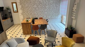 A modern living room with a sofa, ottoman, and chairs, a wooden dining table with chairs, and a kitchen area with cabinets and appliances. - La Bergerie Maison Ancienne Rénovée (Villacerf)