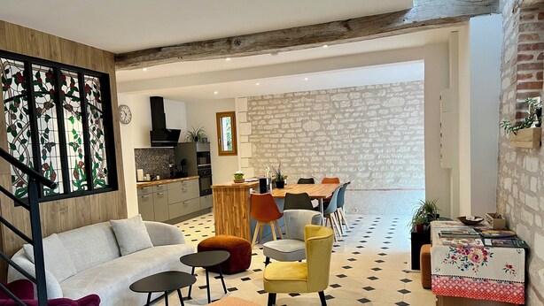 A modern living room with a sofa, ottoman, and coffee table, a dining area with chairs and a table, and a kitchen with a stove and cabinets. - La Bergerie Maison Ancienne Rénovée (Villacerf)