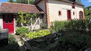 A house with a red door, brick walls, and a garden with various plants. - La Bergerie Maison Ancienne Rénovée (Villacerf)