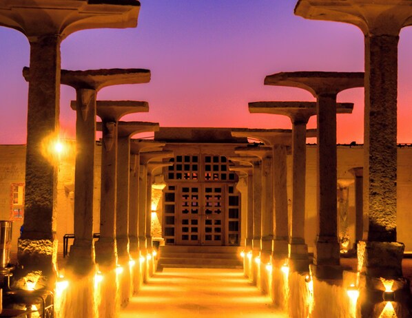 A corridor with columns and a central door, illuminated by lights.