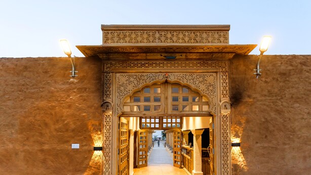 An ornate entrance with intricate carvings and two wall-mounted lights. - Hotel Sia Luxury Resort (Jaisalmer)