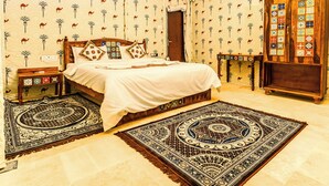 A bedroom with a bed, two nightstands, a wooden wardrobe, and patterned carpets. - Hotel Sia Luxury Resort (Jaisalmer)