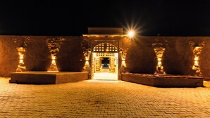 A nighttime view of a courtyard with a central archway, flanked by two large columns, and a paved floor. - Hotel Sia Luxury Resort (Jaisalmer)
