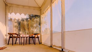 A tented area with two wooden chairs and a table, a view of trees through the window, and a white wall. - Hotel Sia Luxury Resort (Jaisalmer)