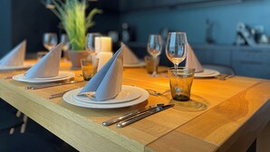 A dining table set with plates, napkins, cutlery, and glasses, with a candle and a plant in the background. - InkBlue Apartment (Heidenau)