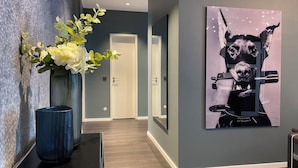 A hallway with a blue vase, a framed artwork of a dog holding a gun, and a door in the background. - InkBlue Apartment (Heidenau)