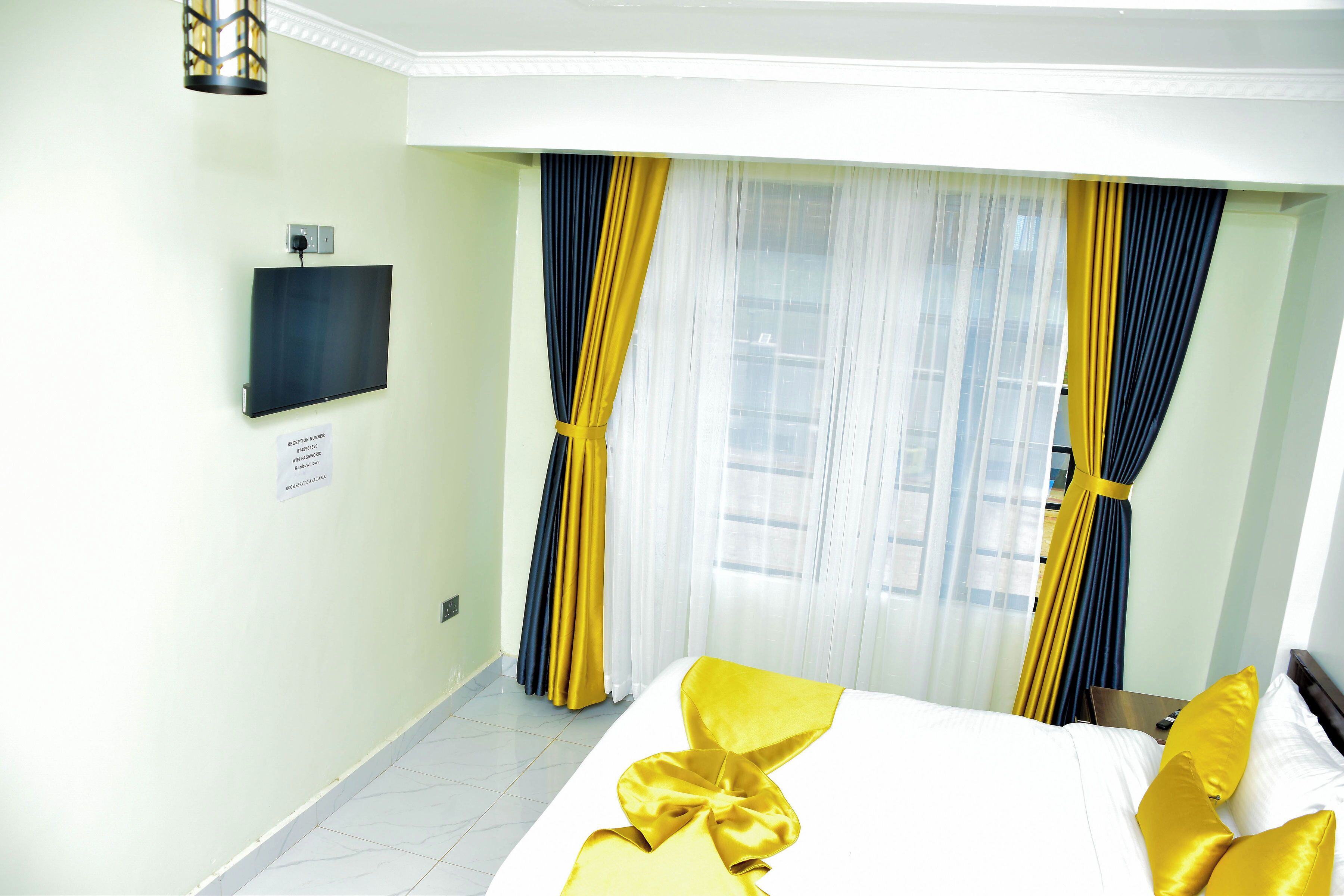 A hotel room with a bed, curtains, a television, and a sign on the wall.