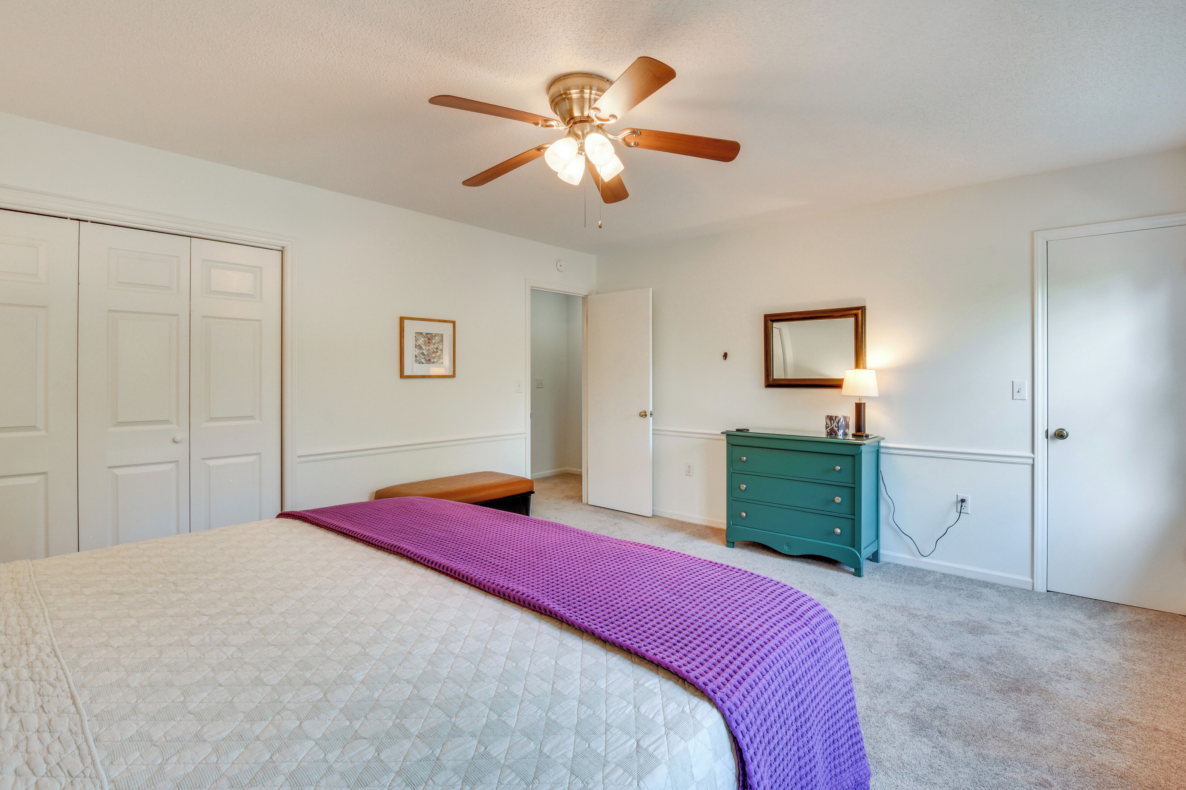 Une chambre à coucher avec un lit, un ventilateur de plafond, une commode et une porte.