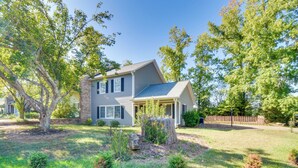 A two-story house with a covered porch, surrounded by a well-maintained lawn and trees. - Screened Patio & Yard: Clemson Weekends/lakes Stay (Seneca)