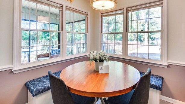 A round wooden table with a flower vase and a WiFi sign, surrounded by blue cushioned benches, in a room with large windows and a hanging light fixture. - Screened Patio & Yard: Clemson Weekends/lakes Stay (Seneca)
