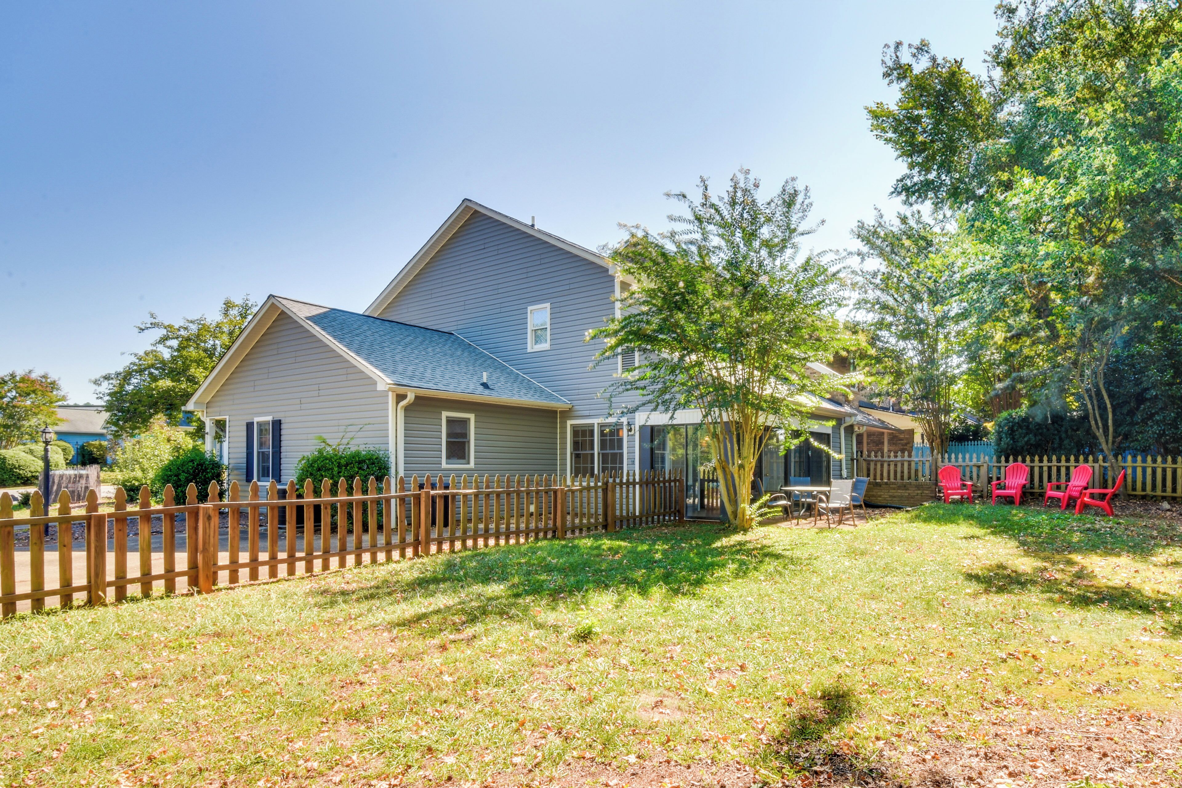 A two-story house with a fenced backyard, a covered patio, and red chairs.