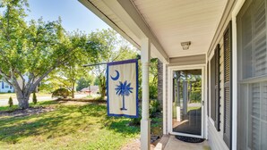 A covered porch with a flag, a tree, and a house entrance. - Screened Patio & Yard: Clemson Weekends/lakes Stay (Seneca)
