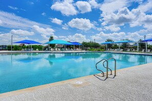 Piscina azul clara con múltiples sombrillas que dan sombra, rodeada de sillones de descanso y una terraza con baldosas.