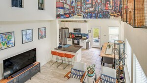 A spacious living area with a large flat-screen TV, a dining table with chairs, and a kitchen in the background. - Large Fenced Yard: Family-friendly Kyle Home (Kyle)