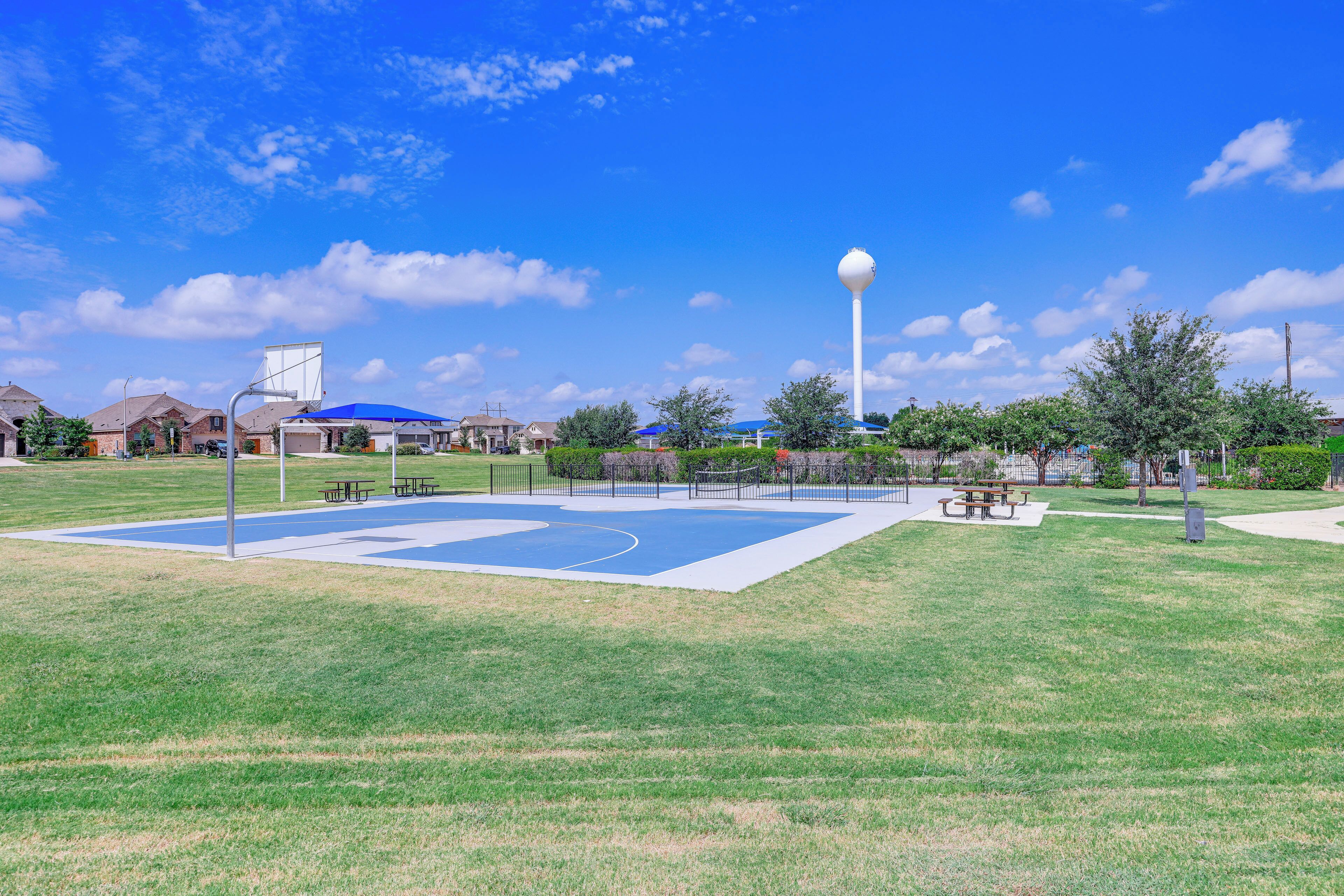 Uma quadra de basquete ao ar livre com mesas de piquenique e um reservatório d'água ao fundo.