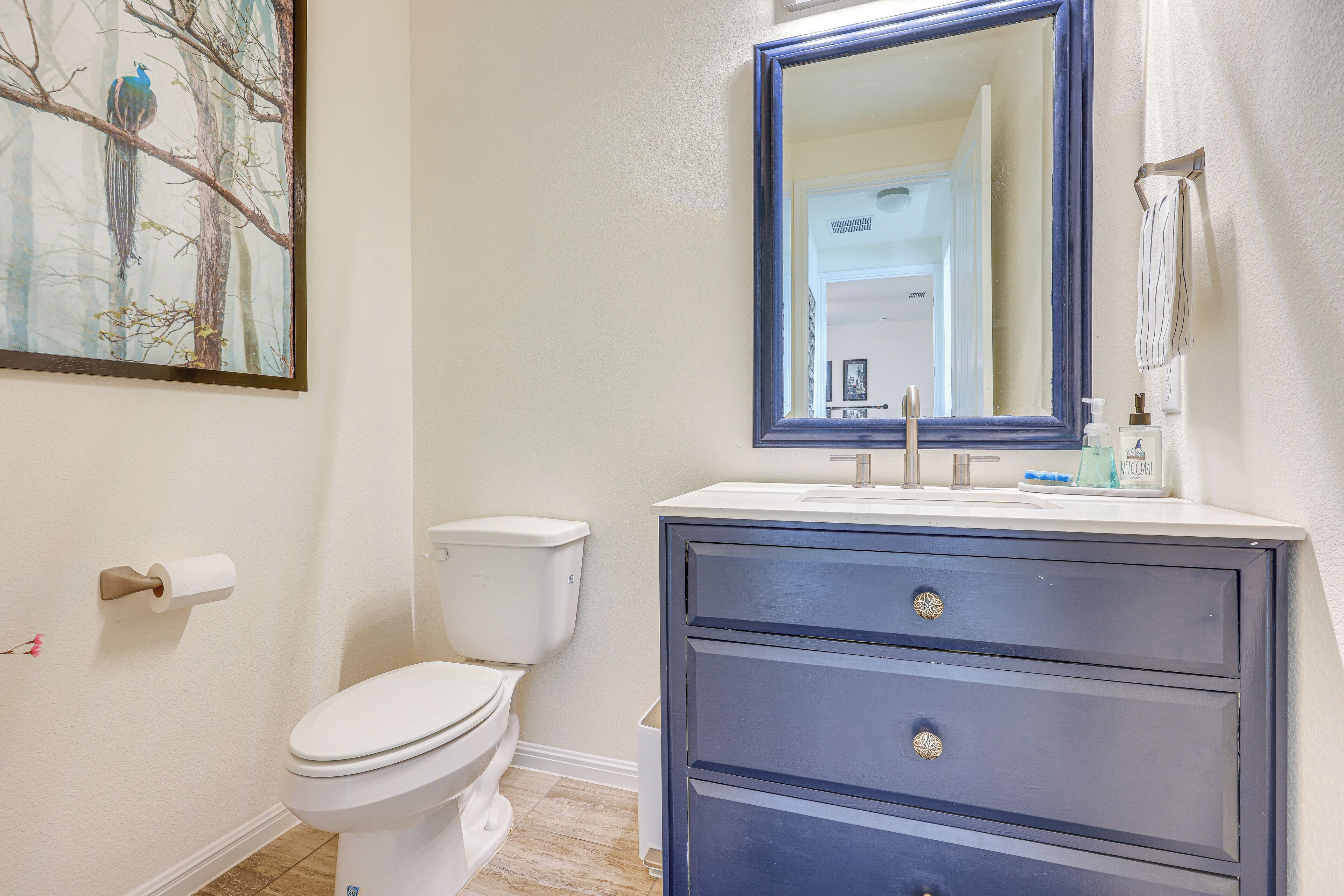 A bathroom with a toilet, a sink with a mirror above it, and a painting on the wall.