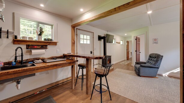Una cocina con encimera de madera, taburetes de bar, estufa y ventana con vistas a árboles.