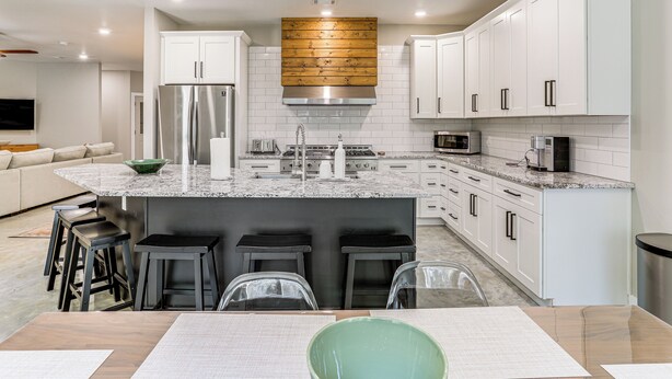 A modern kitchen with white cabinets, a stainless steel refrigerator, a wooden backsplash, and a central island with bar stools. - Spacious Heber Springs Home - Easy Marina Access! (Heber Springs)