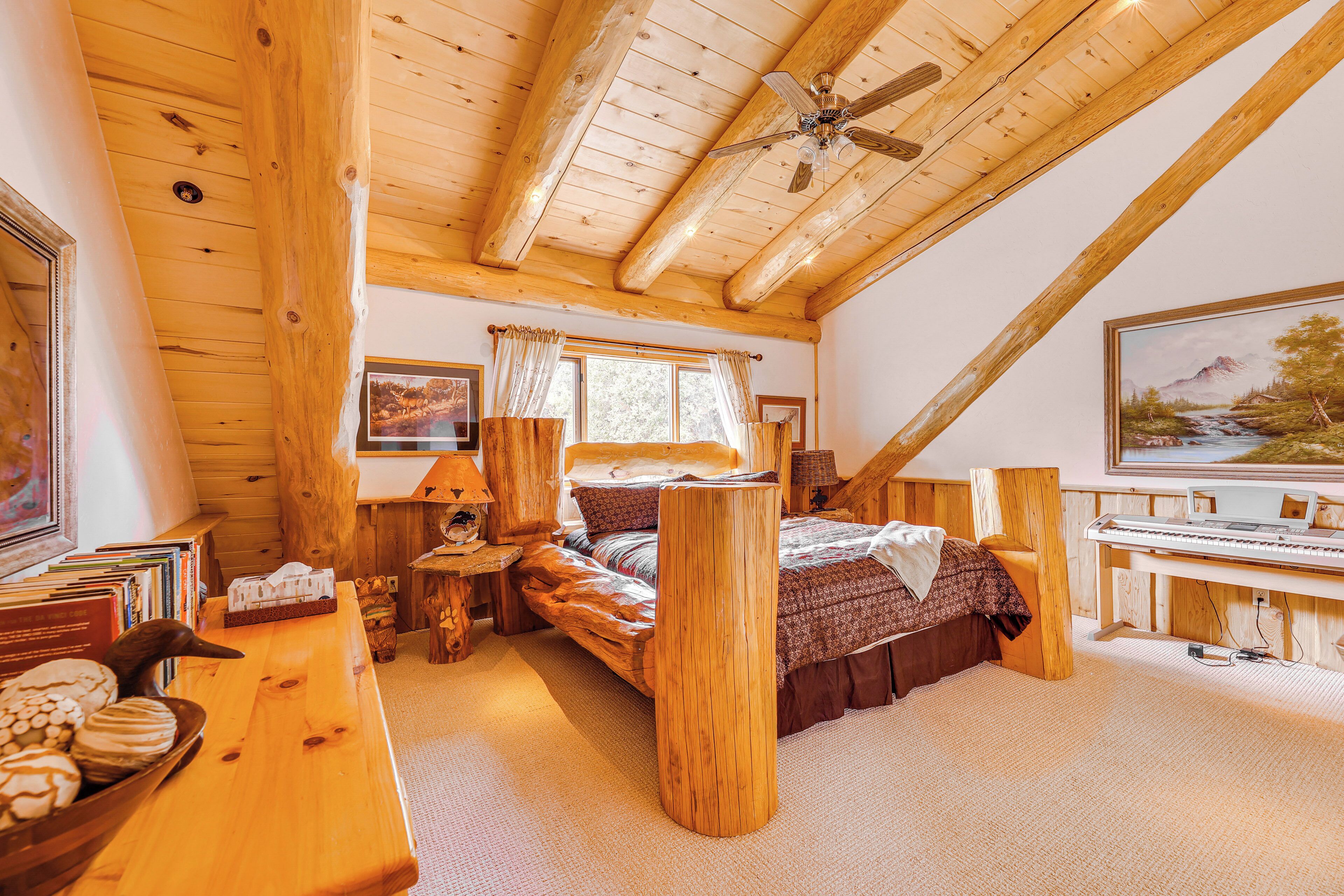 A cozy log cabin bedroom with a bed, wooden furniture, a piano, and a large window.