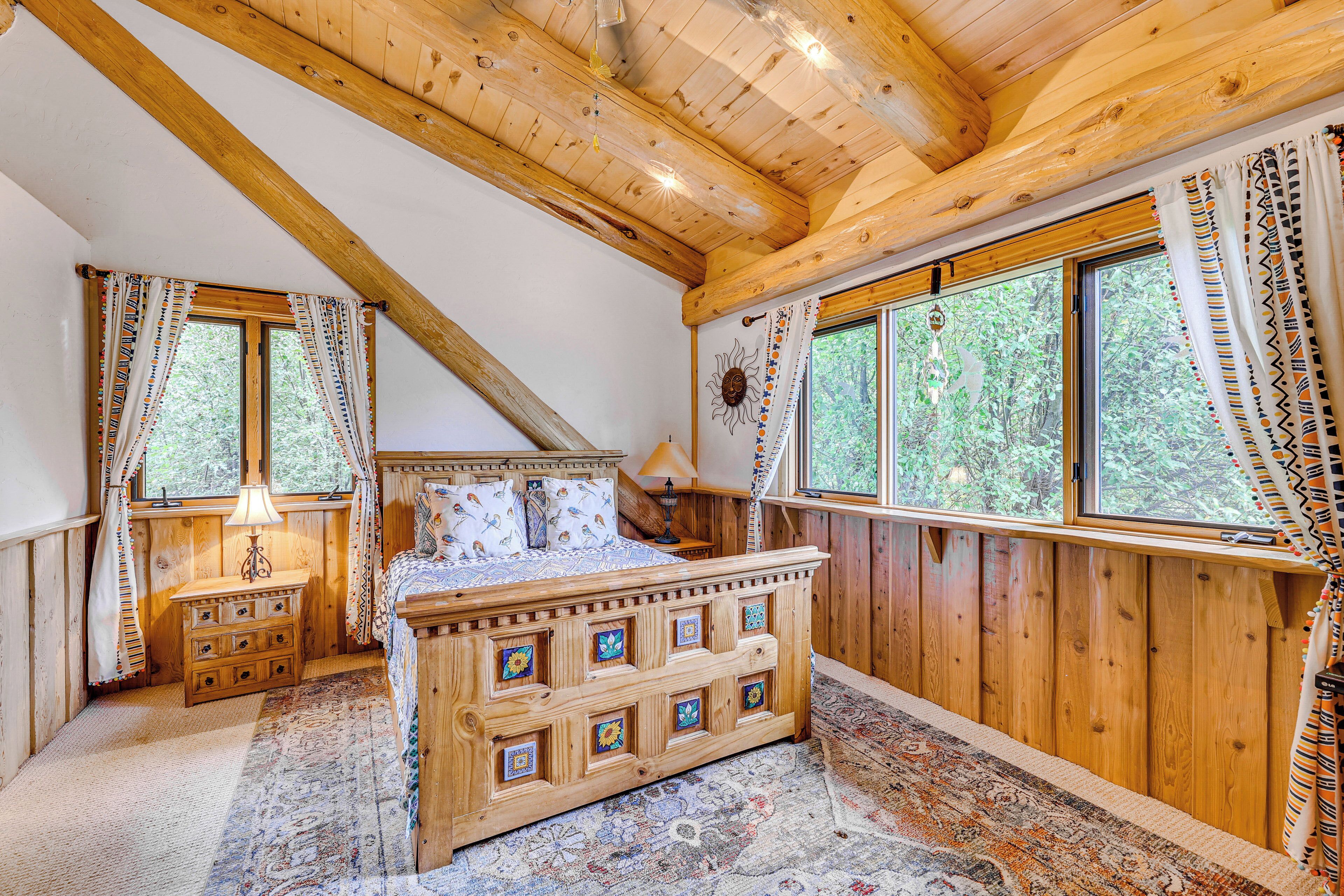 A wooden bedroom with a bed, dresser, and large windows.