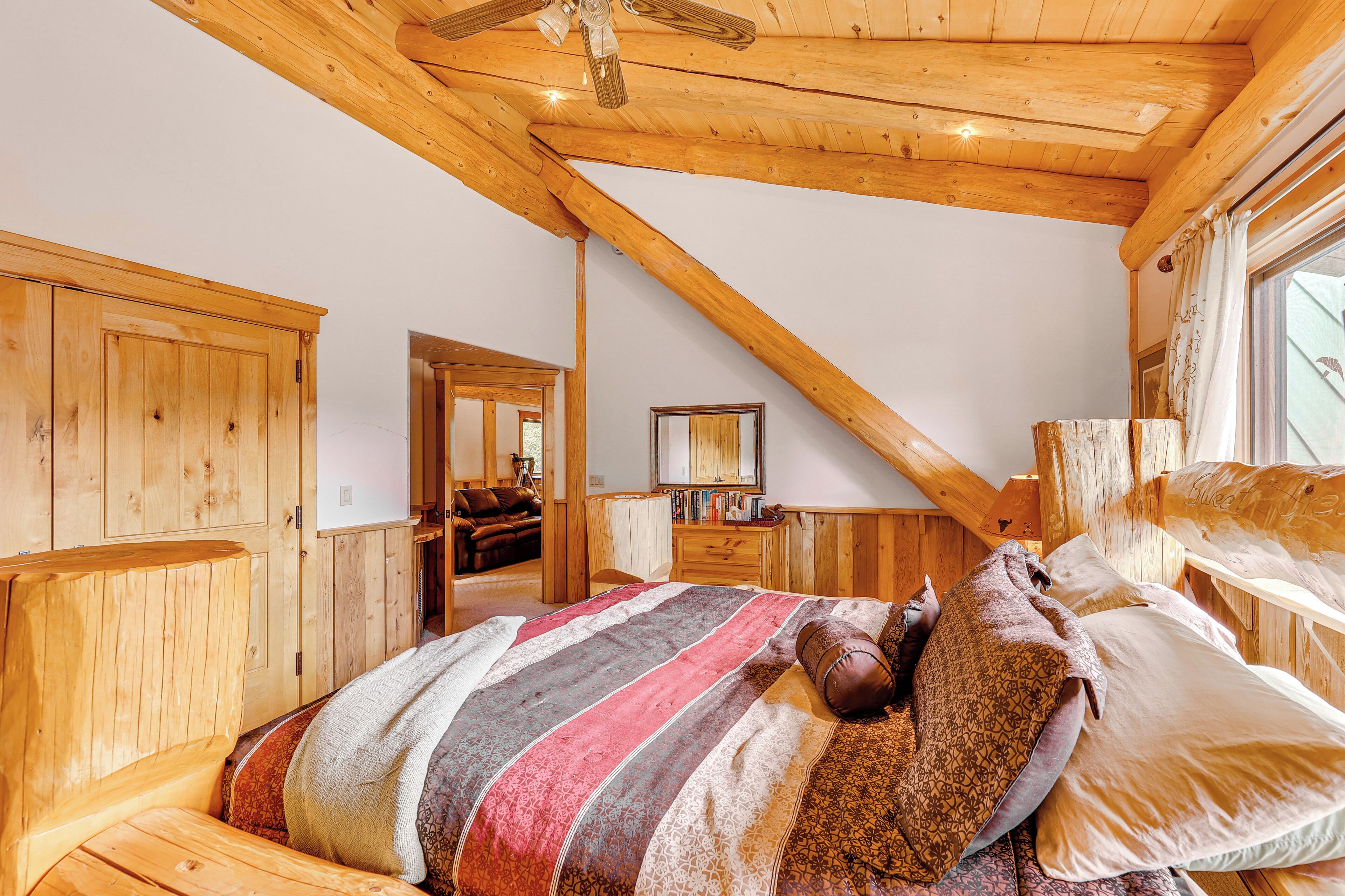 A bedroom with a sloped ceiling, wooden walls, a bed with multiple pillows, and a dresser.