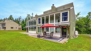 Une maison moderne à deux étages, dotée de grandes fenêtres, d’un patio avec des meubles d’extérieur et d’une pelouse bien entretenue.