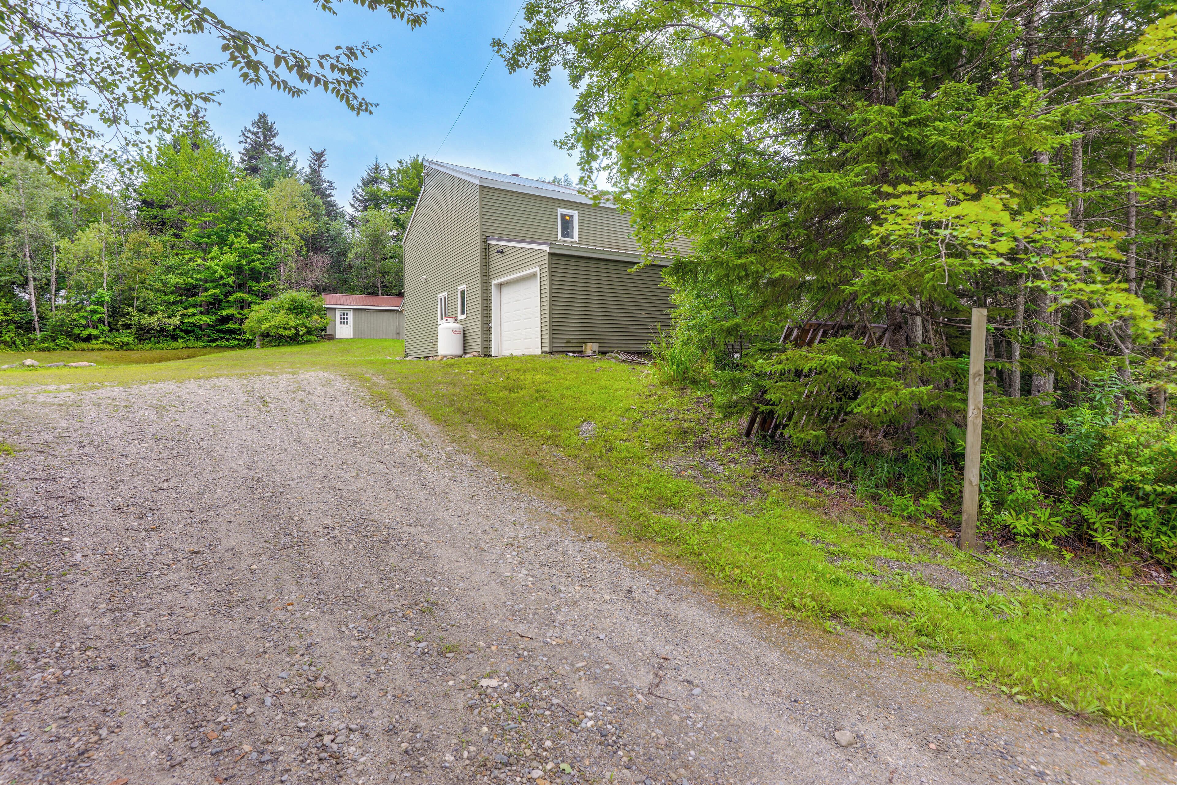 A gravel driveway leading to a single-story house with a garage, surrounded by dense greenery and trees.