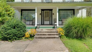 Ein zweistöckiges Haus mit Veranda, Stufen zum Eingang und einem kleinen Garten mit gelben Blumen.