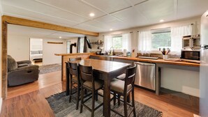 A modern kitchen with a wooden dining table, four chairs, a built-in oven, and a dishwasher. - Private Hot Tub: Main Cabin at Elk Creek Escape! (Hillsgrove)