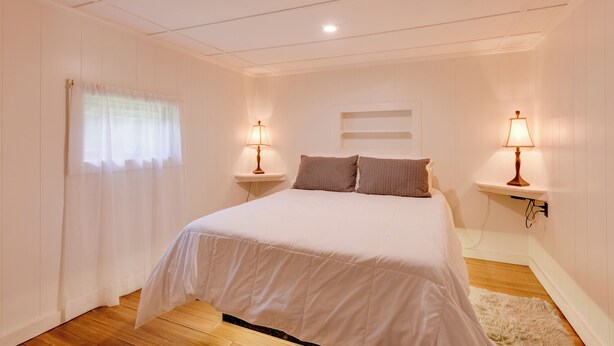 A bedroom with a large bed, two bedside tables with lamps, a window with sheer curtains, and a white wall with a recessed shelf. - Private Hot Tub: Main Cabin at Elk Creek Escape! (Hillsgrove)