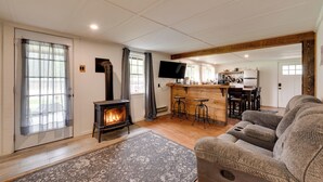 Un salon chaleureux avec une cheminée, un canapé et un coin cuisine à l’arrière-plan.