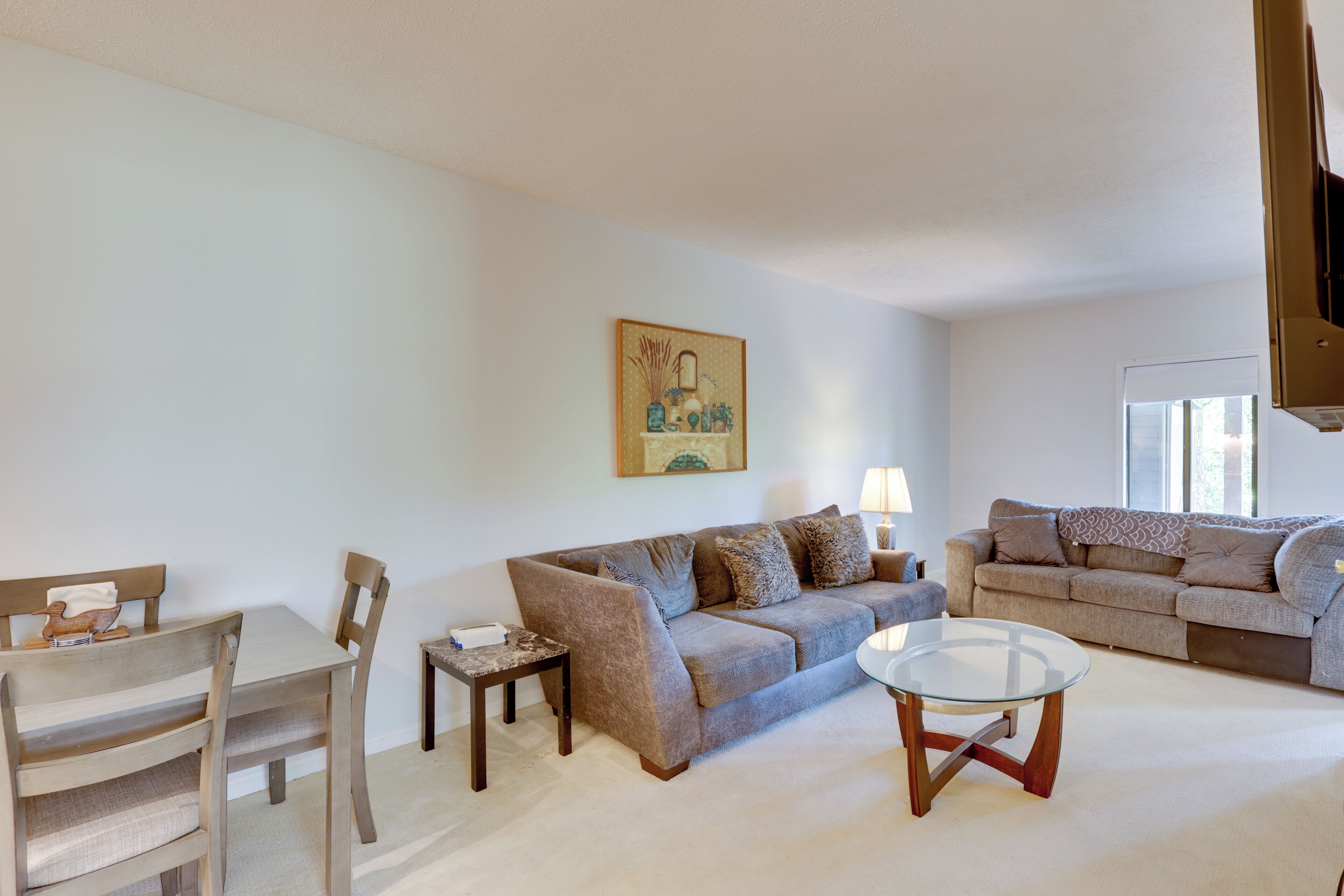 Ein Wohnzimmer mit einer Couch, einem Glastisch, einem Esstisch mit Stühlen und einem Gemälde an der Wand.