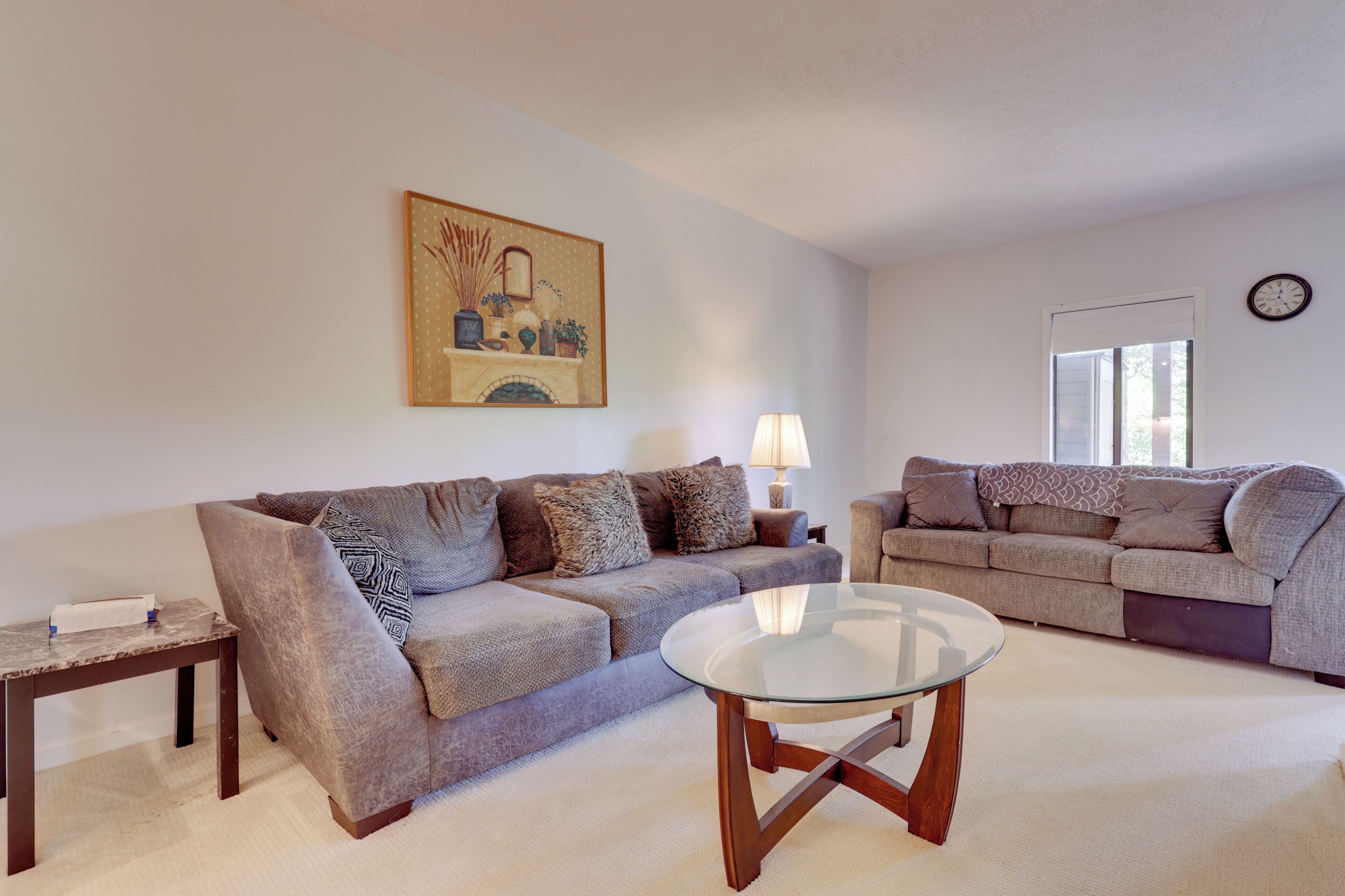 A living room with two sofas, a glass coffee table, a lamp, and a painting on the wall.