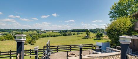 A wooden deck with a view of a green landscape, a fence, and a building with a chimney.