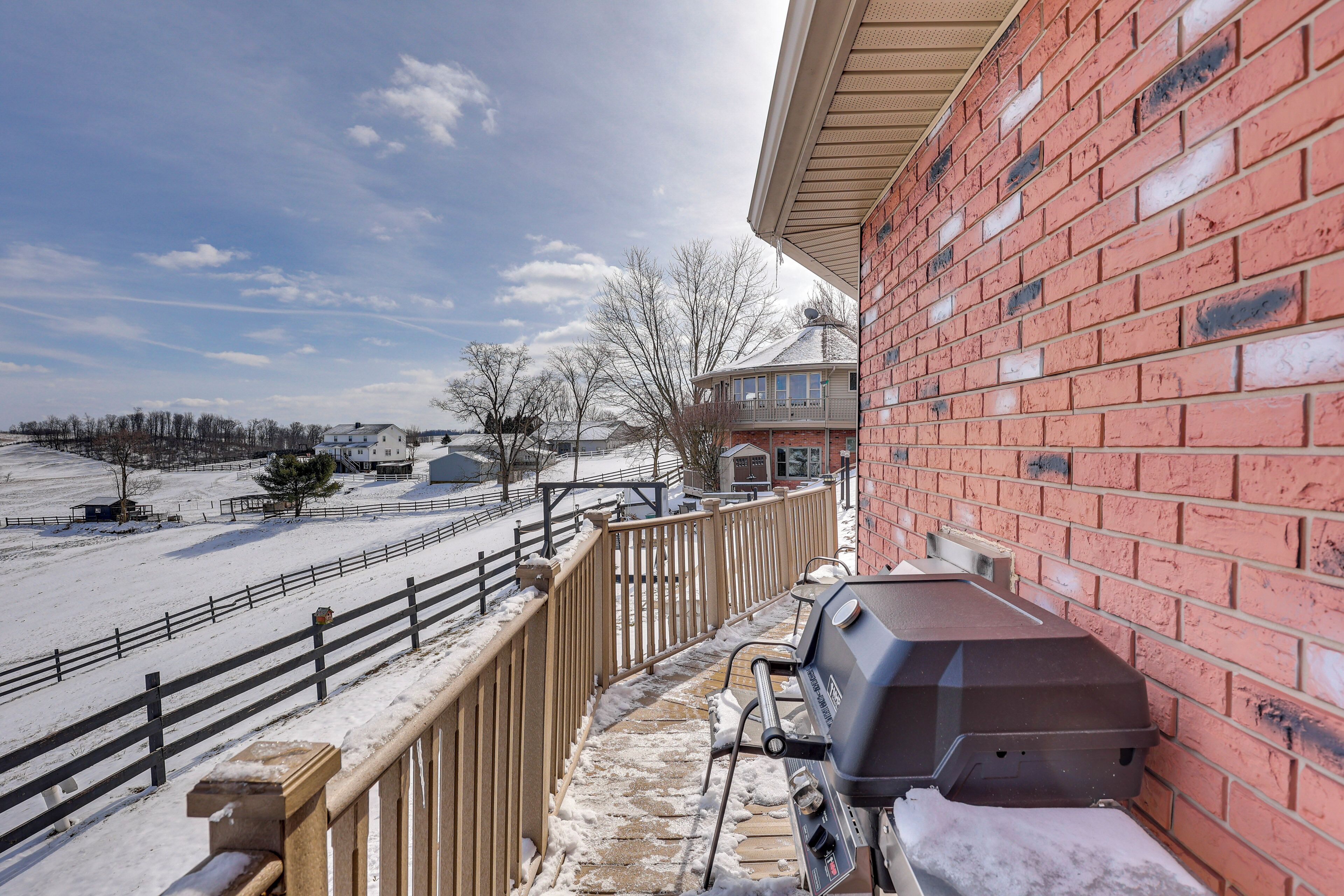 Een balkon met een barbecue, een houten hek en uitzicht op een besneeerd landschap.