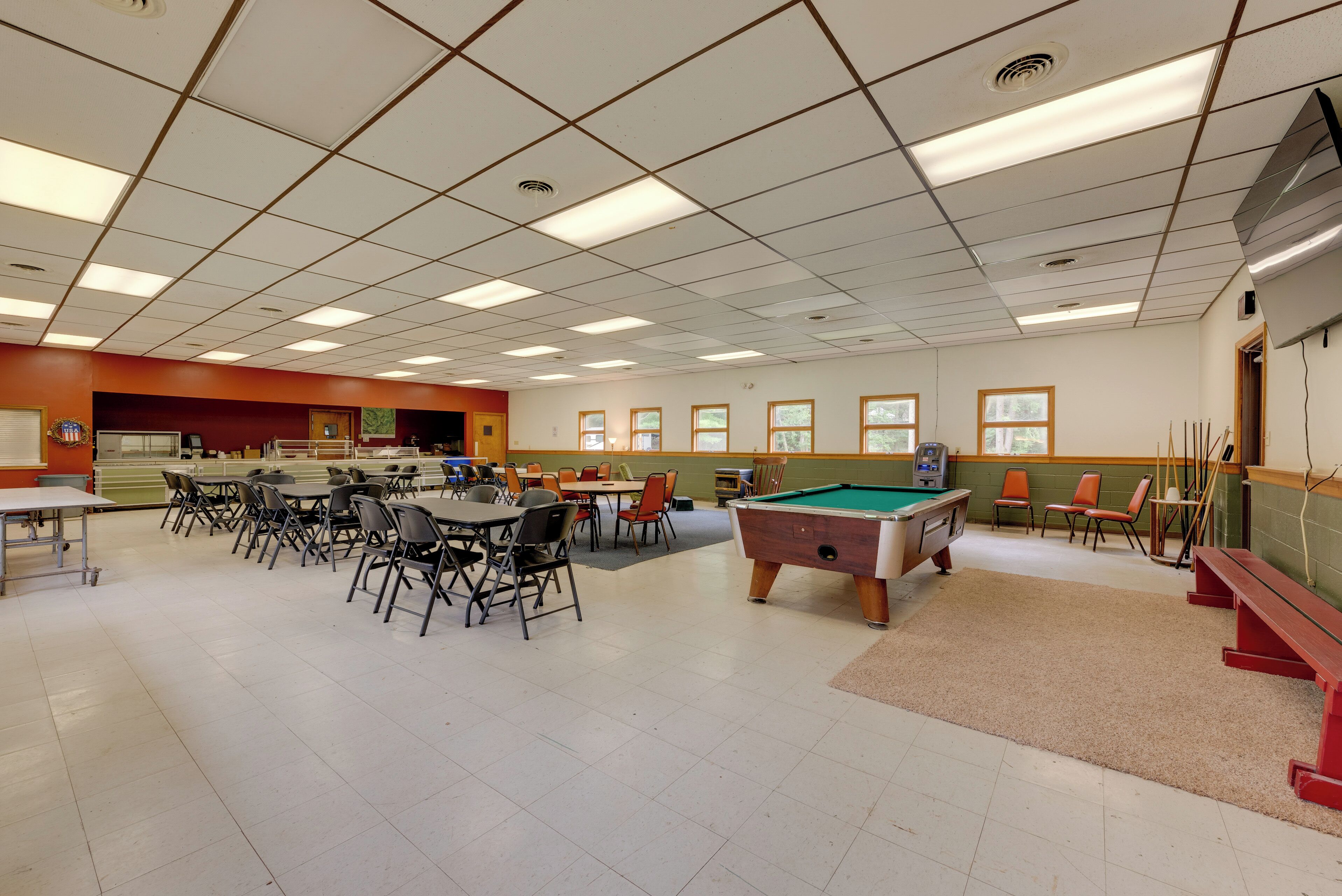 Uma sala de lazer com mesa de bilhar, várias mesas, cadeiras e suporte para tacos.