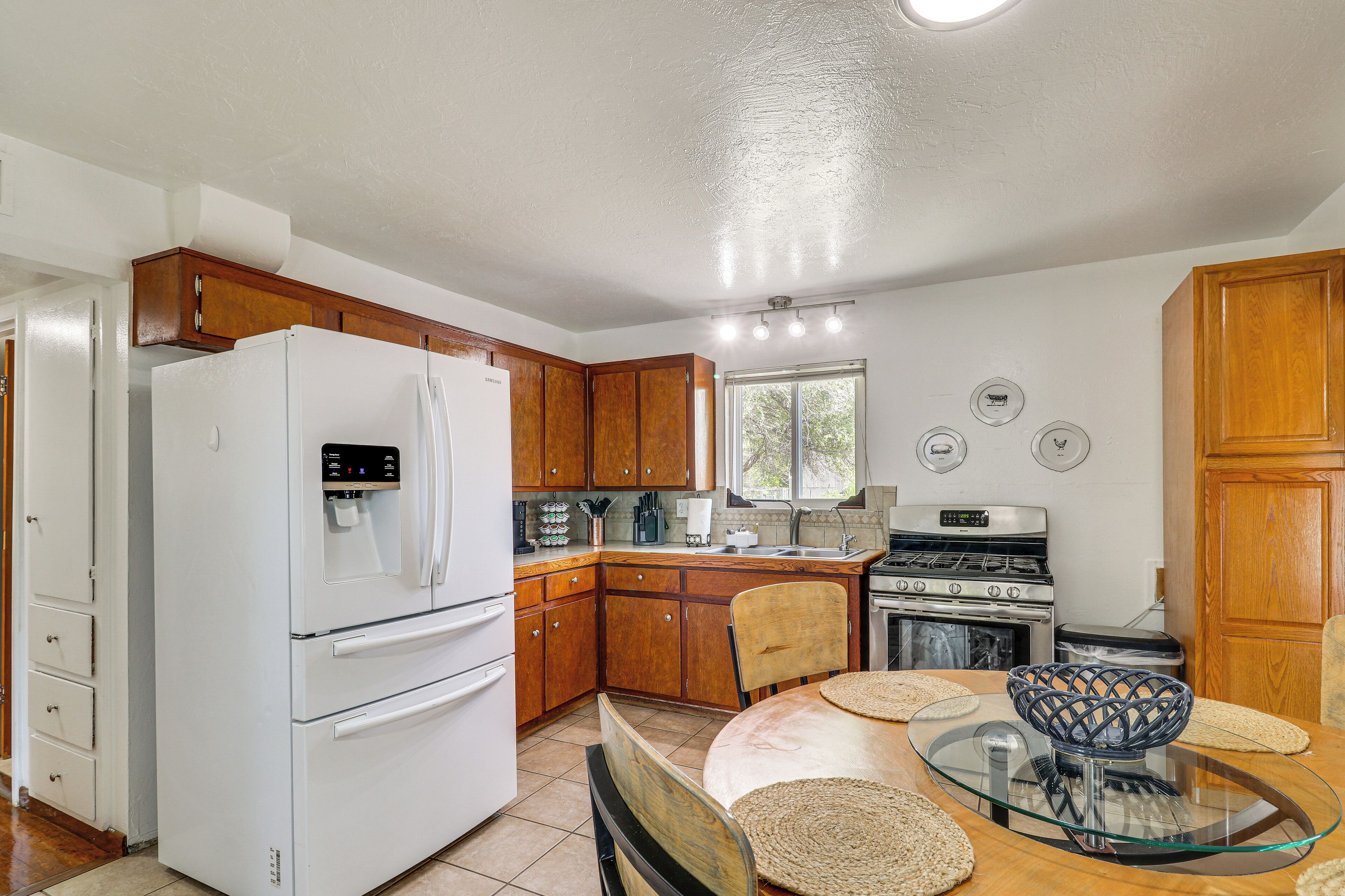 A kitchen with wooden cabinets, a white refrigerator, a stove, and a dining table with a glass top.