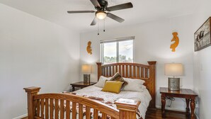 A bedroom with a wooden bed, a ceiling fan, two bedside tables with lamps, and a window with a view. - Family-friendly Albuquerque Home Near Rio Grande! (Albuquerque)