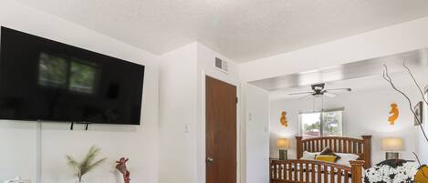 A living room with a TV, wooden console, and a bed with a headboard.