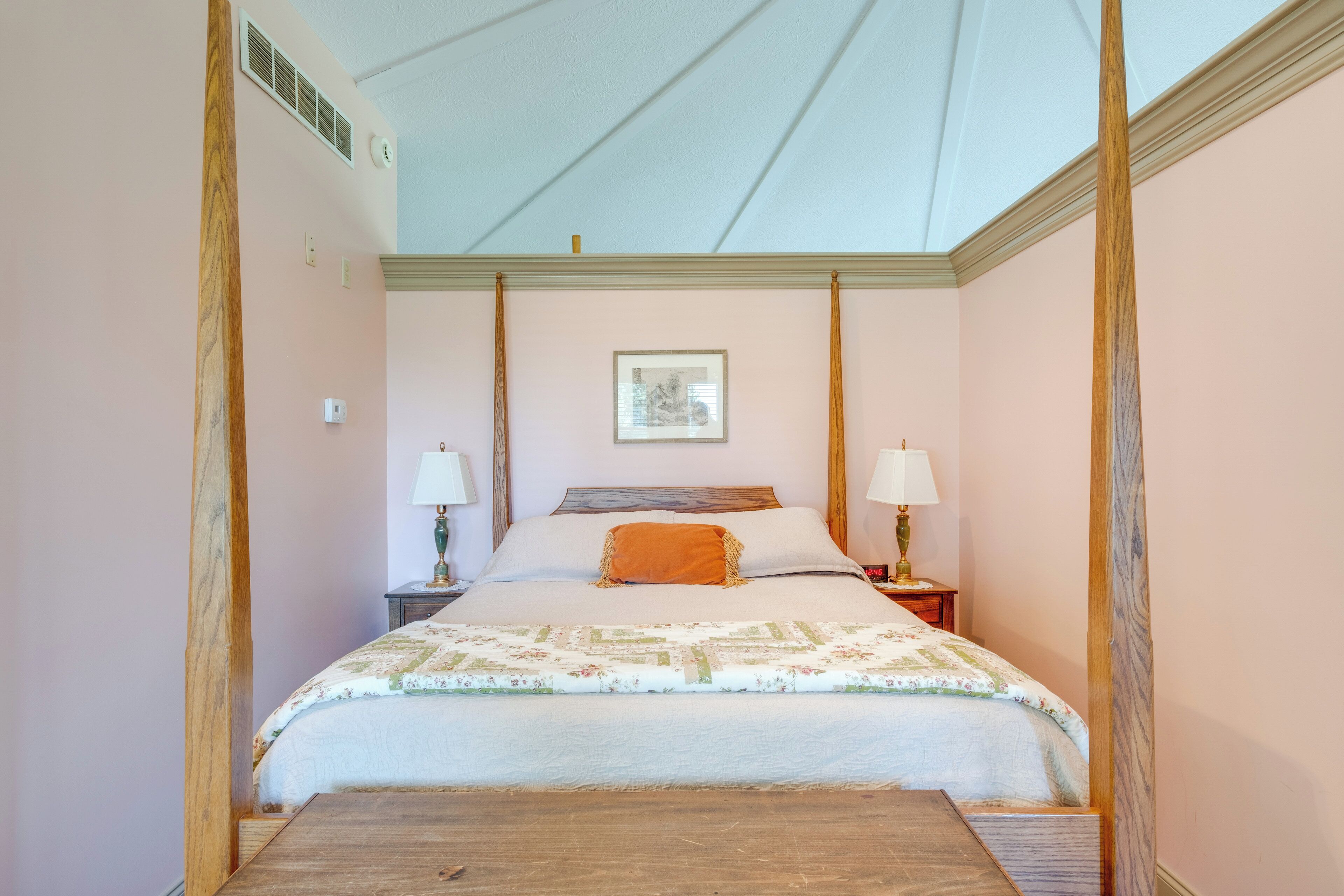 A bedroom with a bed, two bedside tables, a nightstand, a framed picture on the wall, and a wooden floor.