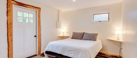 Une chambre avec une porte en bois, un lit avec une literie blanche, deux lampes de chevet, une petite fenêtre et un radiateur fixé au mur.