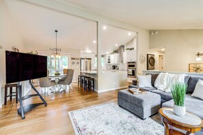 A modern living room with a grey sofa, a TV on a stand, and a dining area with chairs and a table. - Gas BBQ Off Balcony: Fire Pit, Near Parks & Museum (Bremerton)
