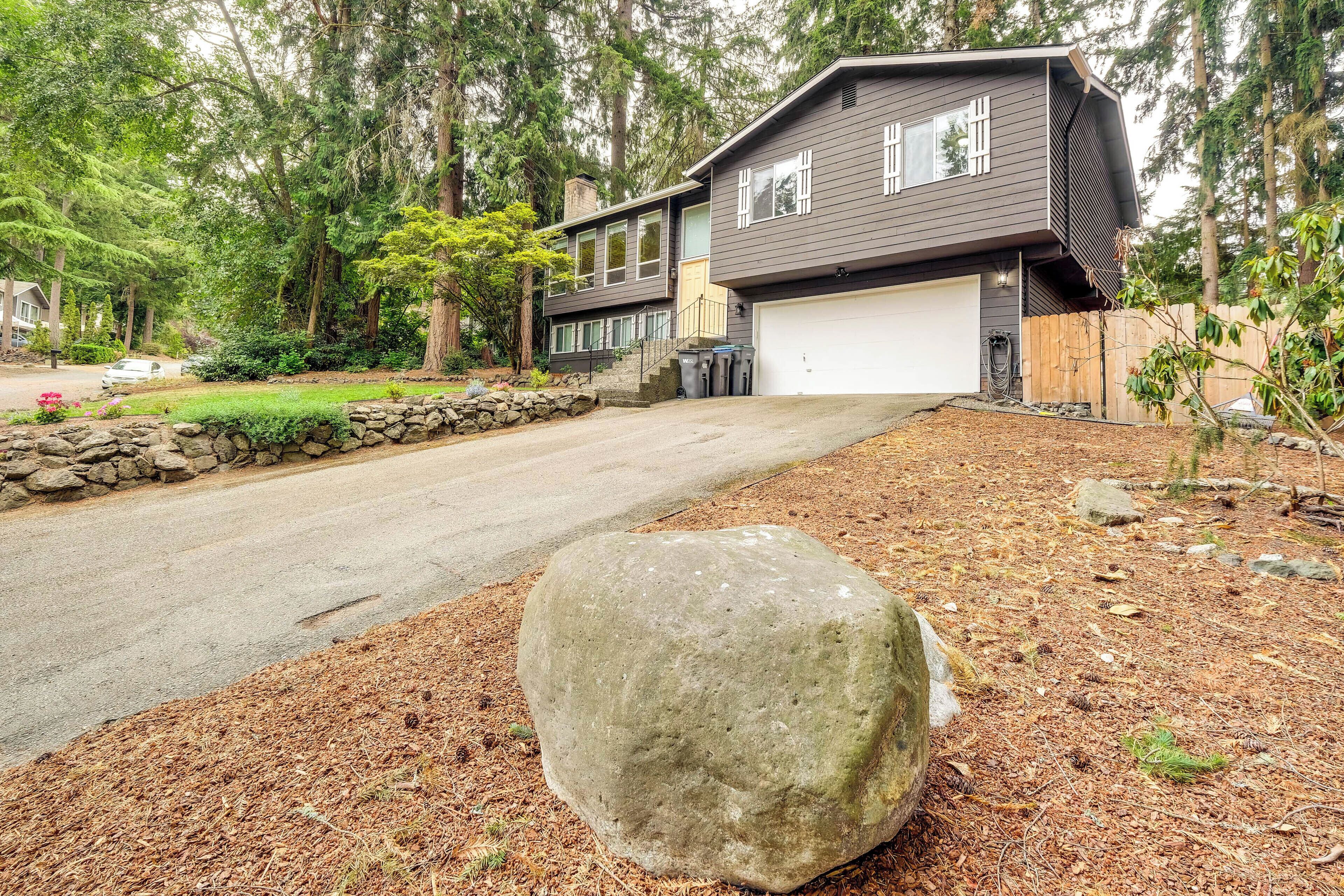 A modern two-story house with a garage, surrounded by a forested area.