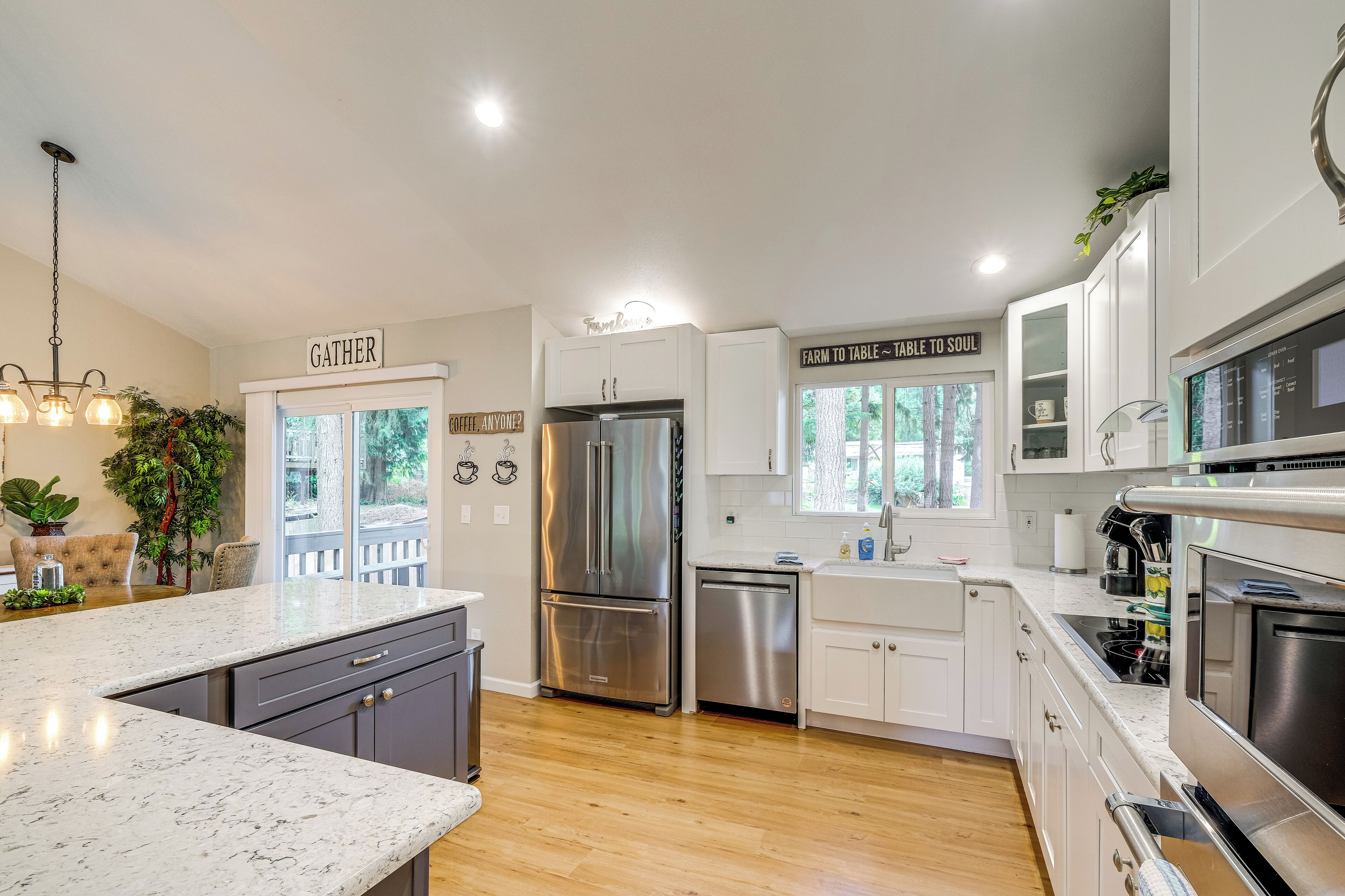 A modern kitchen with white cabinets, stainless steel appliances, a marble countertop, and a sign that reads "GATHER".