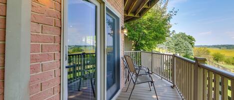 A wooden deck with a glass door leading to a balcony, overlooking a green landscape.