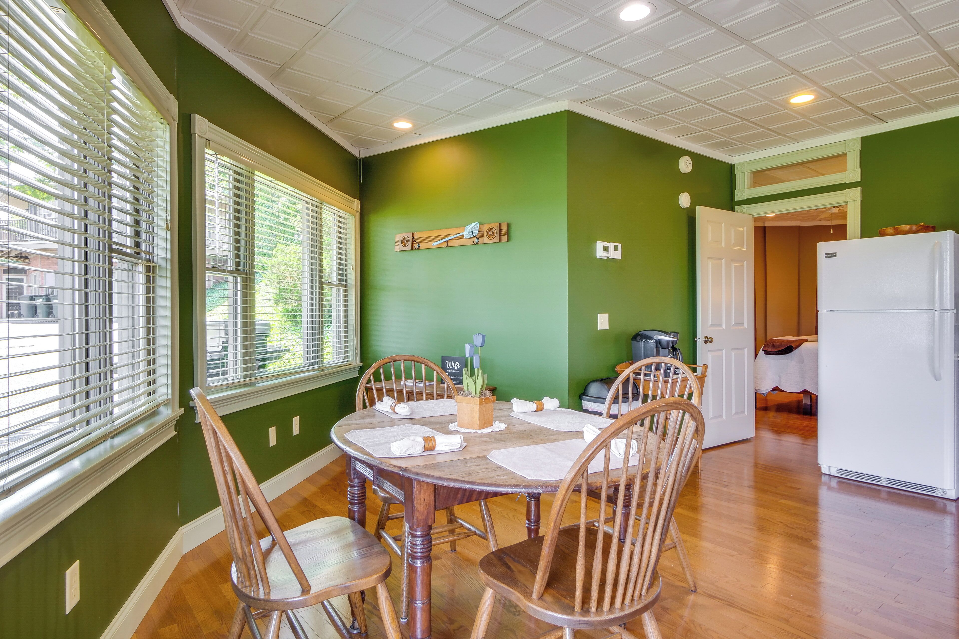 A dining area with a round wooden table and six wooden chairs, a green wall, and a white ceiling.